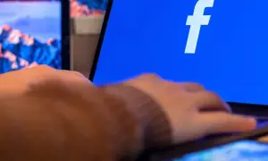 Dłoń na telefonie, obok ekranu laptopa z logo Facebooka. Dowiedz się, jak zaktualizować Facebooka na telefonie, by cieszyć się nowymi funkcjami.