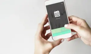 Dłonie trzymające smartfon z ikoną kalendarza i napisem "History" na ekranie.