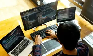 Programista pracuje przy biurku z trzema ekranami, pokazując, jak używać laptopa jako monitora.