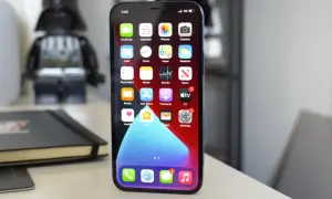 iPhone 11 z widocznym wskaźnikiem 5G na ekranie, na biurku obok figurki Dartha Vadera.