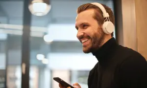 Uśmiechnięty mężczyzna w słuchawkach JBL trzyma iPhone'a, gotowy do połączenia.