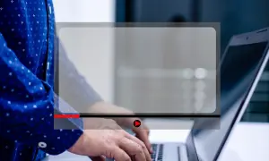 Osoba pisze na laptopie, a na ekranie widoczny jest odtwarzacz wideo. Dowiedz się, jak zmniejszyć ekran w przeglądarce, aby wygodniej oglądać.