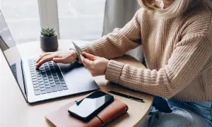 Kobieta z kartą płatniczą przy laptopie, szuka informacji, jak sprawdzić numer karty w aplikacji IKO.