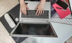 Ręce piszą na laptopie, obok telefon i czerwona książka. Zastanawiasz się, jaki laptop kupić do domu?