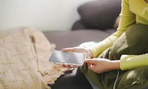 Osoba podłącza iPhone'a do ładowania, co jest kluczowe, jak dbać o baterie iPhone. Niska bateria na ekranie telefonu.