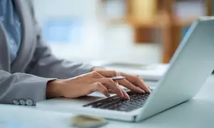 Dłonie piszą na klawiaturze laptopa, zastanawiając się, ile prądu zużywa laptop na godzinę.