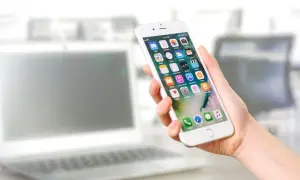Dłoń trzyma iPhone'a z widocznymi ikonami aplikacji. Dowiedz się, jak odinstalować aplikacje, aby zwolnić miejsce.