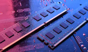 Dwa moduły RAM do laptopa leżą na płycie głównej, oświetlone niebieskim i różowym światłem.