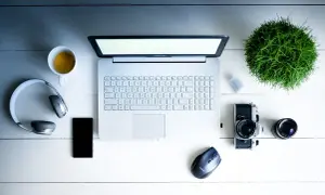 Na biurku leży laptop, słuchawki, telefon, aparat i filiżanka kawy. Dowiedz się, jak włączyć dźwięk w laptopie na klawiaturze.