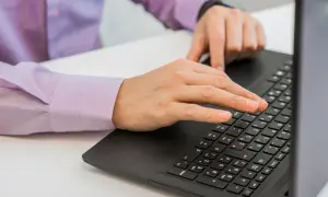 Dłonie piszące na klawiaturze laptopa.