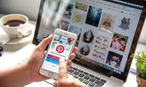 Osoba korzysta z telefonu z aplikacją Pinterest, sprawdzając, czy aplikacja Pinterest jest darmowa. Na ekranie telefonu widnieje logo Pinterest i opcje logowania.