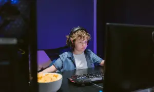 Chłopiec w słuchawkach gra w Roblox na przeglądarce, obok miska chipsów.
