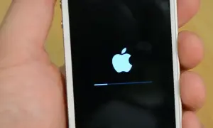 Dłoń trzyma biały iPhone z logo Apple i paskiem postępu. To ekran, który pojawia się, gdy próbujesz jak zresetować iPhone.