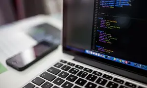 Laptop z kodem na ekranie i telefonem w tle.