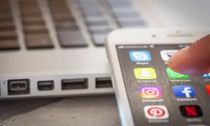 Palec dotyka ikony WhatsApp na ekranie smartfona, obok laptopa. To pokazuje, jak app cloud ułatwia dostęp do komunikatorów.