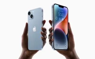 Dwie ręce trzymają jasnoniebieskie iPhone'y 14. Zastanawiasz się, czy oplaca sie kupic iPhone 14?