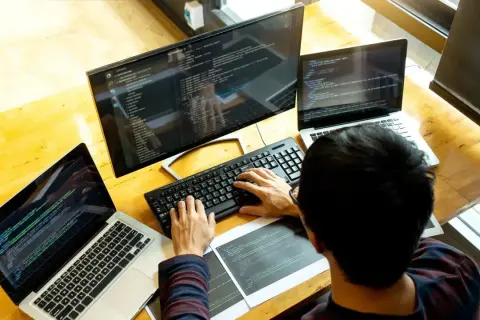 Programista pracuje przy biurku z trzema ekranami, pokazując, jak używać laptopa jako monitora.