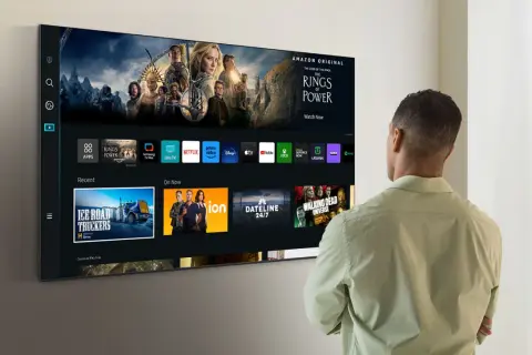 Mężczyzna patrzy na nowoczesny telewizor Samsung z interfejsem Smart TV i ikonami aplikacji.