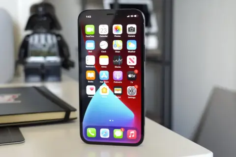 iPhone 11 z widocznym wskaźnikiem 5G na ekranie, na biurku obok figurki Dartha Vadera.