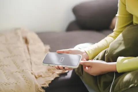 Osoba podłącza iPhone'a do ładowania, co jest kluczowe, jak dbać o baterie iPhone. Niska bateria na ekranie telefonu.