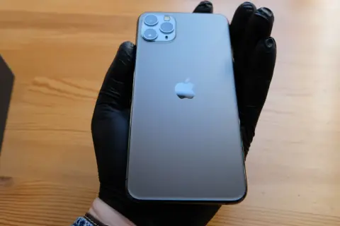 Szary iPhone 11 Pro z potrójnym aparatem, trzymany w czarnej rękawiczce.