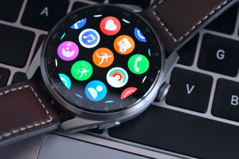 Huawei Watch z kolorowymi ikonami aplikacji na ekranie, leżący na klawiaturze. Dowiedz się, jak zaktualizować Huawei Watch, by cieszyć się nowymi funkcjami.