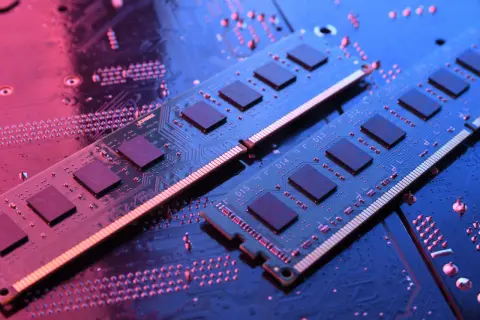 Dwa moduły RAM do laptopa leżą na płycie głównej, oświetlone niebieskim i różowym światłem.