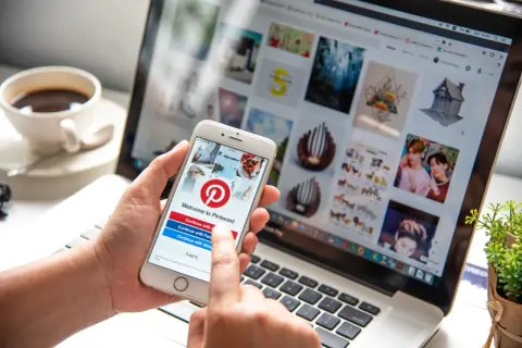 Osoba korzysta z telefonu z aplikacją Pinterest, sprawdzając, czy aplikacja Pinterest jest darmowa. Na ekranie telefonu widnieje logo Pinterest i opcje logowania.