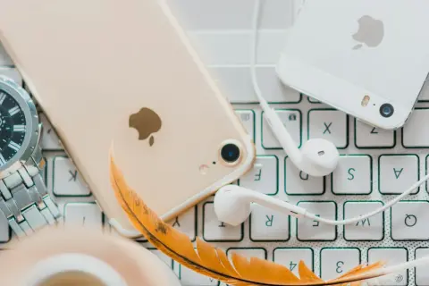 Złoty iPhone, białe słuchawki i piórko na klawiaturze – idealne akcesoria do słuchania audiobooków. Jaka aplikacja do audiobooków sprawdzi się najlepiej?