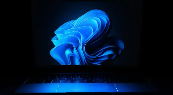 Laptop z niebieskim podświetleniem klawiatury i ekranem z abstrakcyjnym motywem. Dowiedz się, jak ustawić hasło na laptopa, by chronić swoje dane.