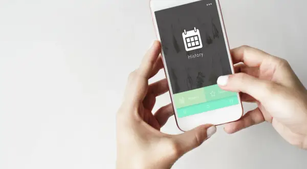 Dłonie trzymające smartfon z ikoną kalendarza i napisem "History" na ekranie.