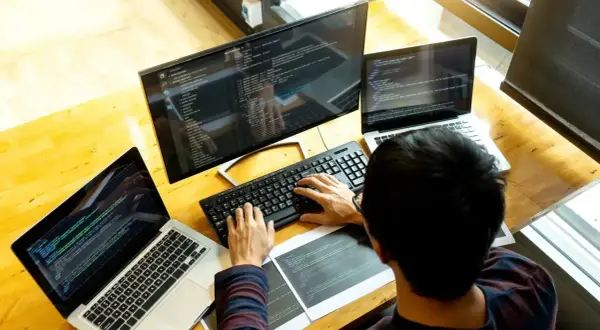 Programista pracuje przy biurku z trzema ekranami, pokazując, jak używać laptopa jako monitora.