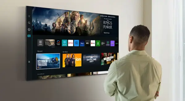 Mężczyzna patrzy na nowoczesny telewizor Samsung z interfejsem Smart TV i ikonami aplikacji.