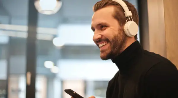 Uśmiechnięty mężczyzna w słuchawkach JBL trzyma iPhone'a, gotowy do połączenia.
