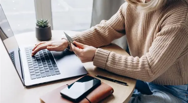 Kobieta z kartą płatniczą przy laptopie, szuka informacji, jak sprawdzić numer karty w aplikacji IKO.