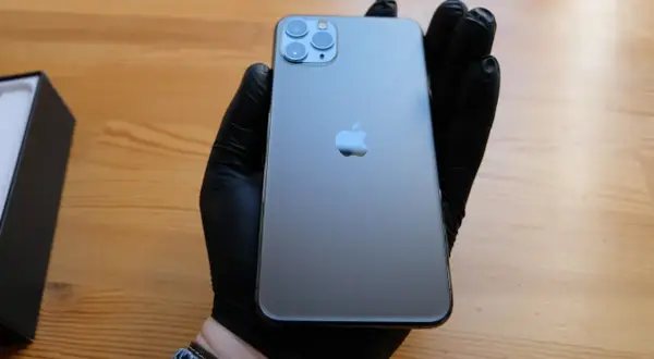 Szary iPhone 11 Pro z potrójnym aparatem, trzymany w czarnej rękawiczce.