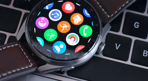 Huawei Watch z kolorowymi ikonami aplikacji na ekranie, leżący na klawiaturze. Dowiedz się, jak zaktualizować Huawei Watch, by cieszyć się nowymi funkcjami.