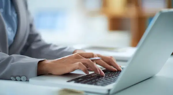 Dłonie piszą na klawiaturze laptopa, zastanawiając się, ile prądu zużywa laptop na godzinę.