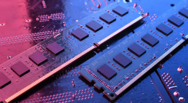 Dwa moduły RAM do laptopa leżą na płycie głównej, oświetlone niebieskim i różowym światłem.