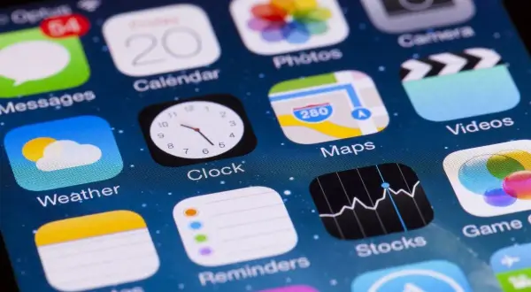 Ekran iPhone'a z ikonami aplikacji, w tym "Stocks", która pokazuje wykresy, sugerując, jakie aplikacje są płatne na iPhone.