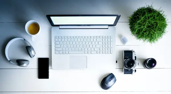 Na biurku leży laptop, słuchawki, telefon, aparat i filiżanka kawy. Dowiedz się, jak włączyć dźwięk w laptopie na klawiaturze.