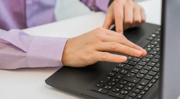 Dłonie piszące na klawiaturze laptopa.