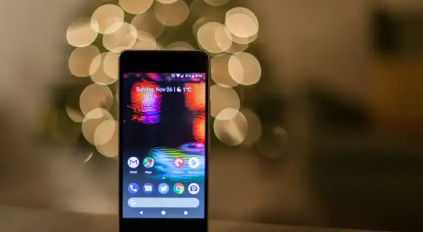 Smartfon z kolorową tapetą i ikonami aplikacji na tle rozmytych światełek.