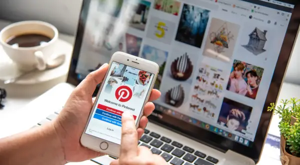 Osoba korzysta z telefonu z aplikacją Pinterest, sprawdzając, czy aplikacja Pinterest jest darmowa. Na ekranie telefonu widnieje logo Pinterest i opcje logowania.