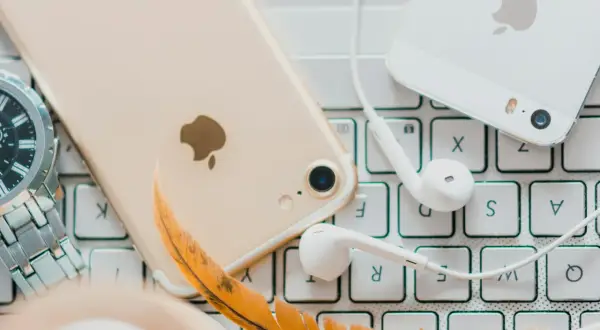 Złoty iPhone, białe słuchawki i piórko na klawiaturze – idealne akcesoria do słuchania audiobooków. Jaka aplikacja do audiobooków sprawdzi się najlepiej?