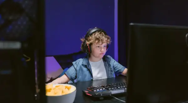 Chłopiec w słuchawkach gra w Roblox na przeglądarce, obok miska chipsów.
