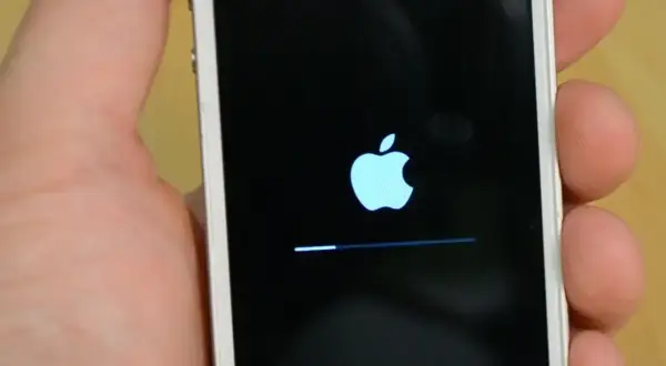 Dłoń trzyma biały iPhone z logo Apple i paskiem postępu. To ekran, który pojawia się, gdy próbujesz jak zresetować iPhone.