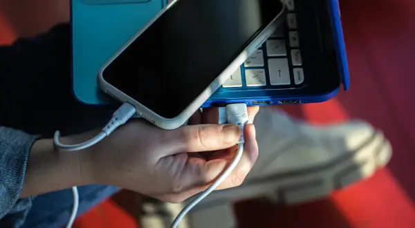 Dłoń podłącza kabel USB telefonu do laptopa, pokazując, jak połączyć telefon z laptopem.