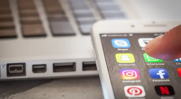 Palec dotyka ikony WhatsApp na ekranie smartfona, obok laptopa. To pokazuje, jak app cloud ułatwia dostęp do komunikatorów.