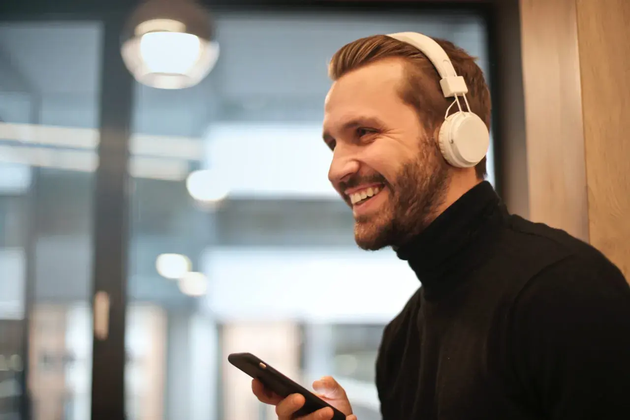 Uśmiechnięty mężczyzna w słuchawkach JBL trzyma iPhone'a, gotowy do połączenia.